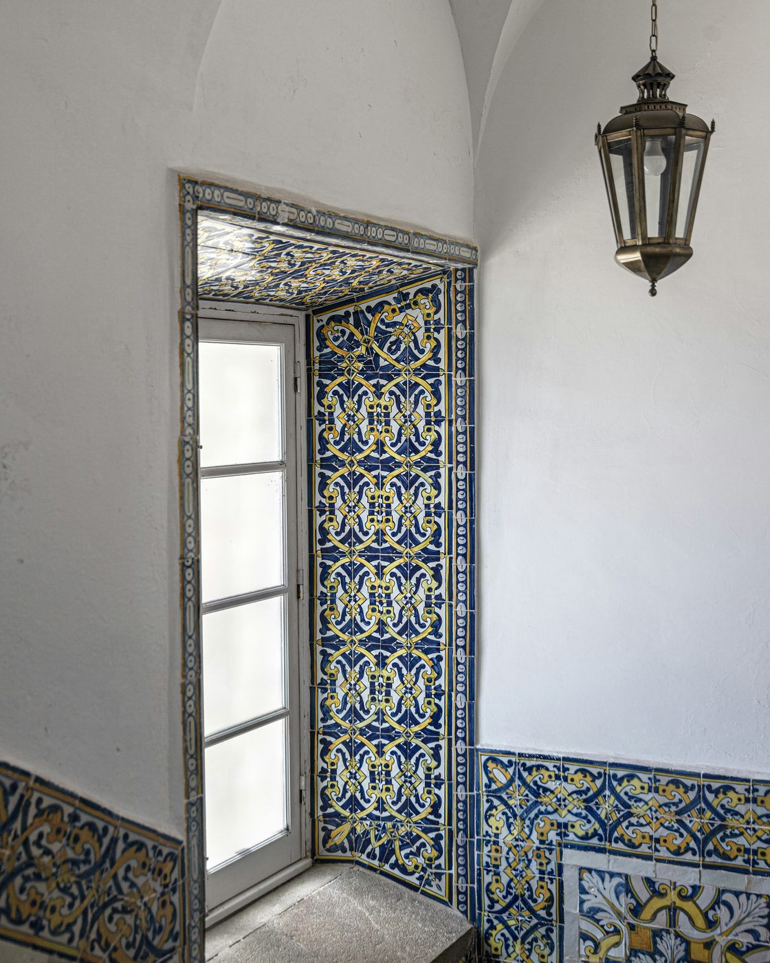 A whitewashed vaulted room with its window reveal tiled in blue and yellow