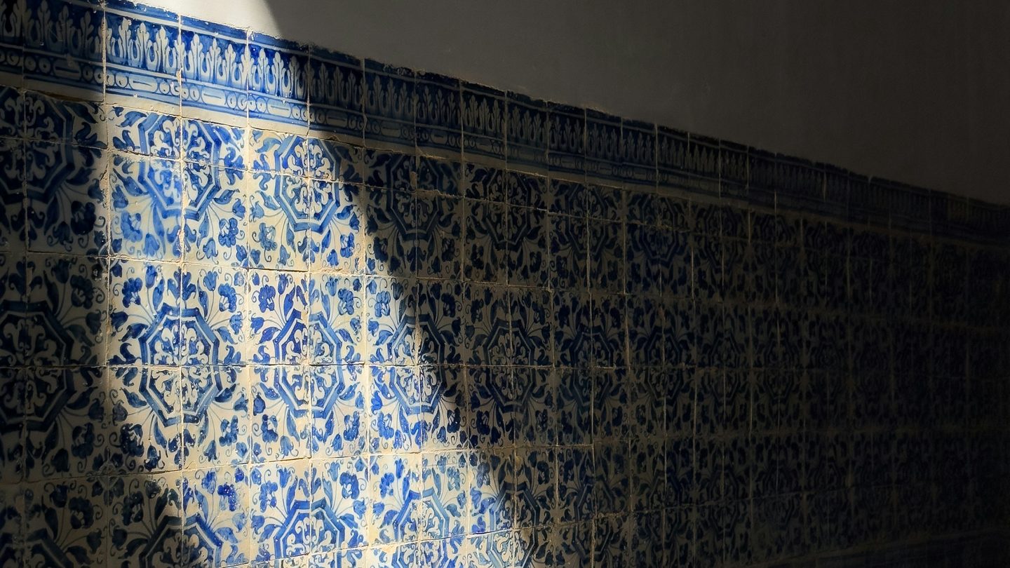 A shaft of daylight across a wall of old blue and white patterned tiles