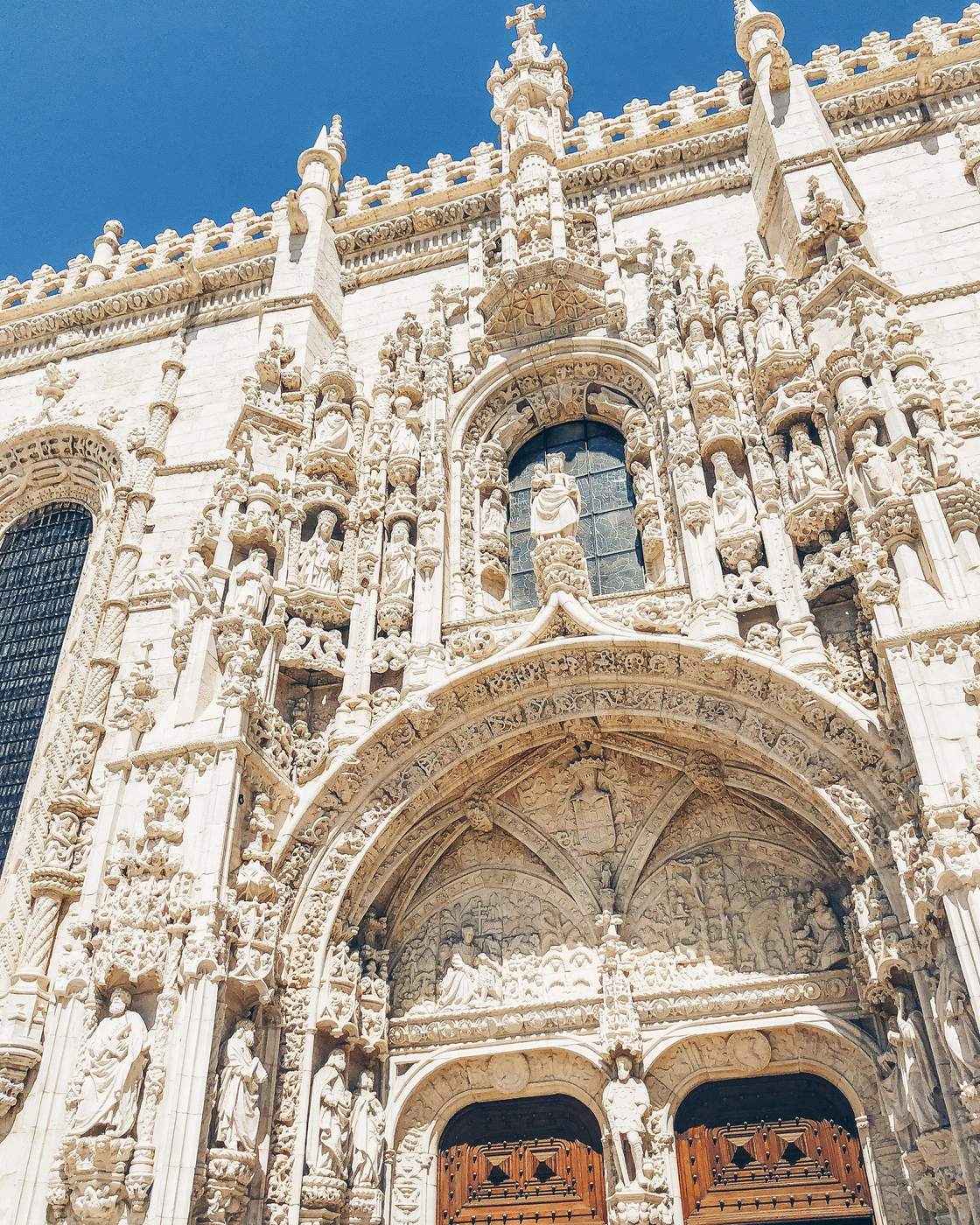The carved white stone south portal of the Jeronimos Monastery in Lisbon against a blue sky