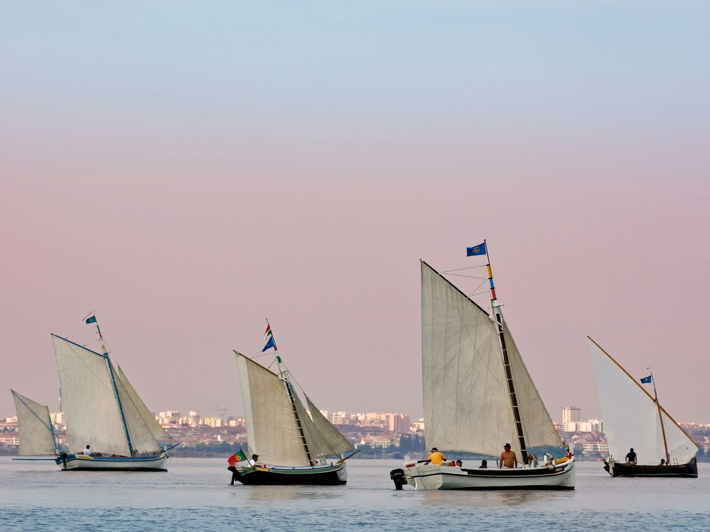 Traditional sailing boats on the Tagus at dusk, with Lisbon on the far bank